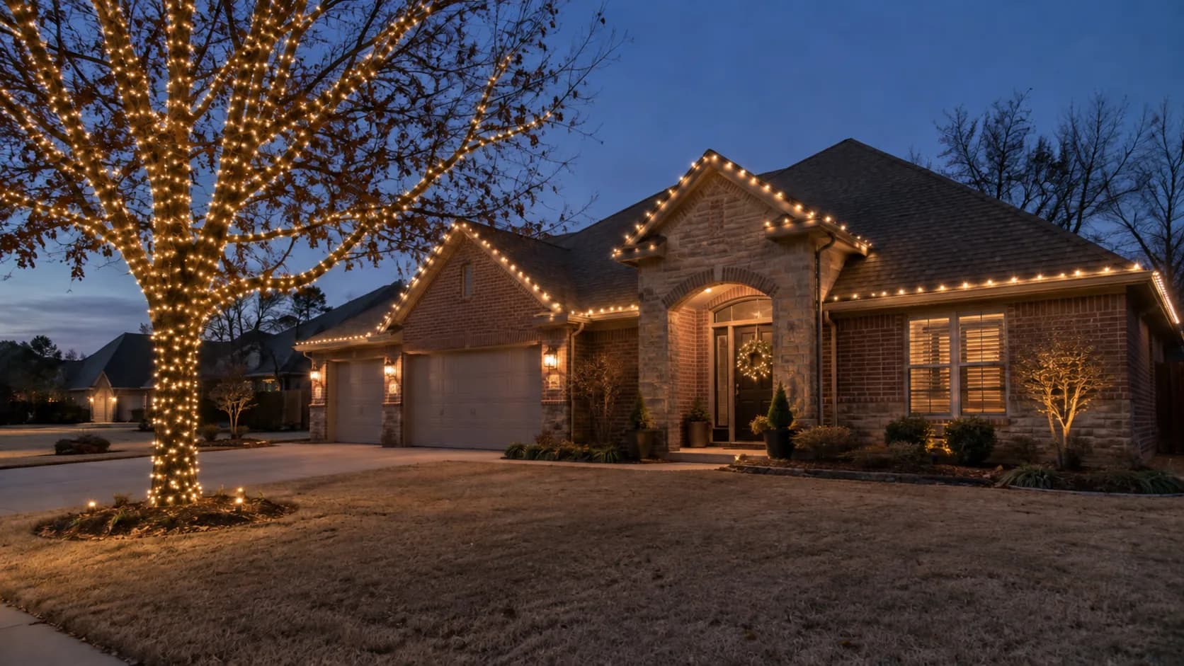 Warm-white roofline lights and an oak wrapped from its trunk up the main branches beside a brick house.